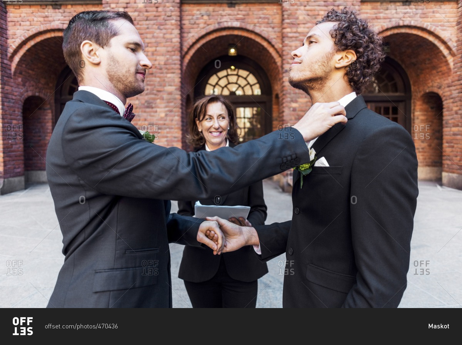 Man adjusting bow tie of gay partner in front of priest during wedding ceremony