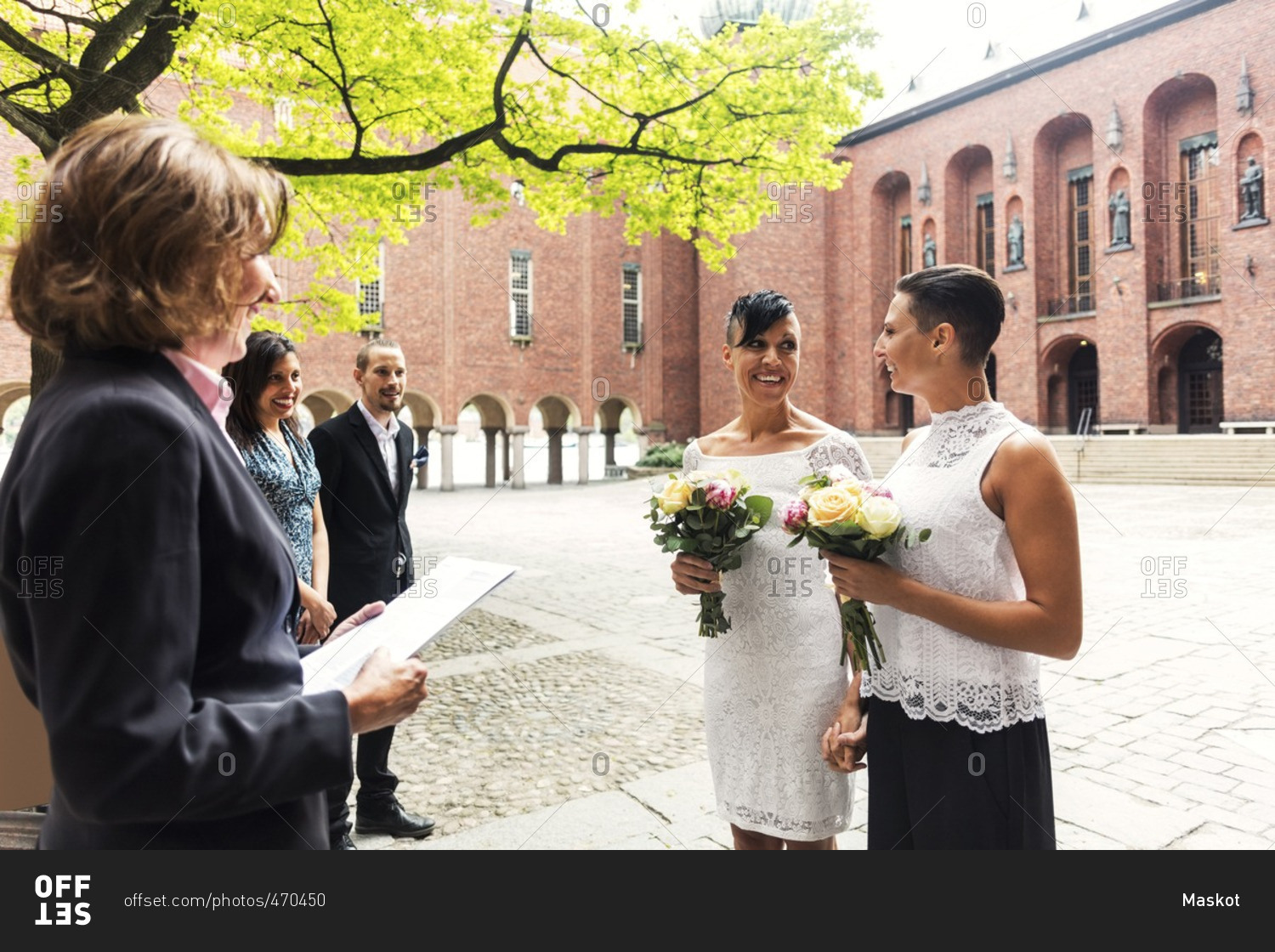 Happy lesbian couple standing in front of female priest for wedding ceremony
