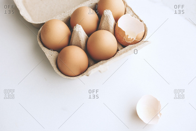 Close up of a half a dozen eggs in a carton with one cracked