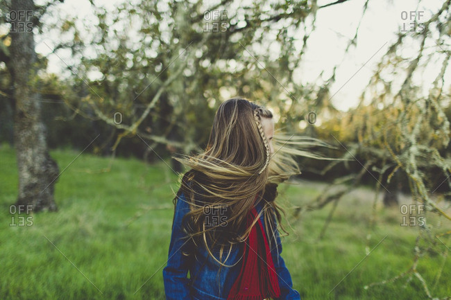 Girl with windblown hair standing in grass with trees
