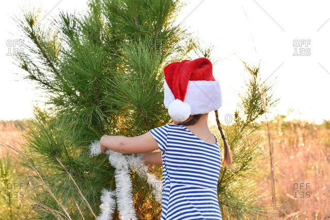 Girl putting Christmas tinsel on outdoor tree
