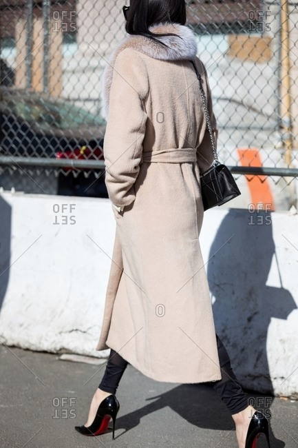 Woman in a long coat and high heels walking on a sidewalk