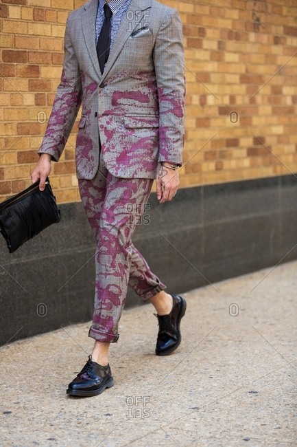 Man in a gray suit with purple stains walking on a sidewalk
