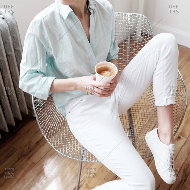 Woman in a blue button-down and shirt sitting in a wire chair with coffee