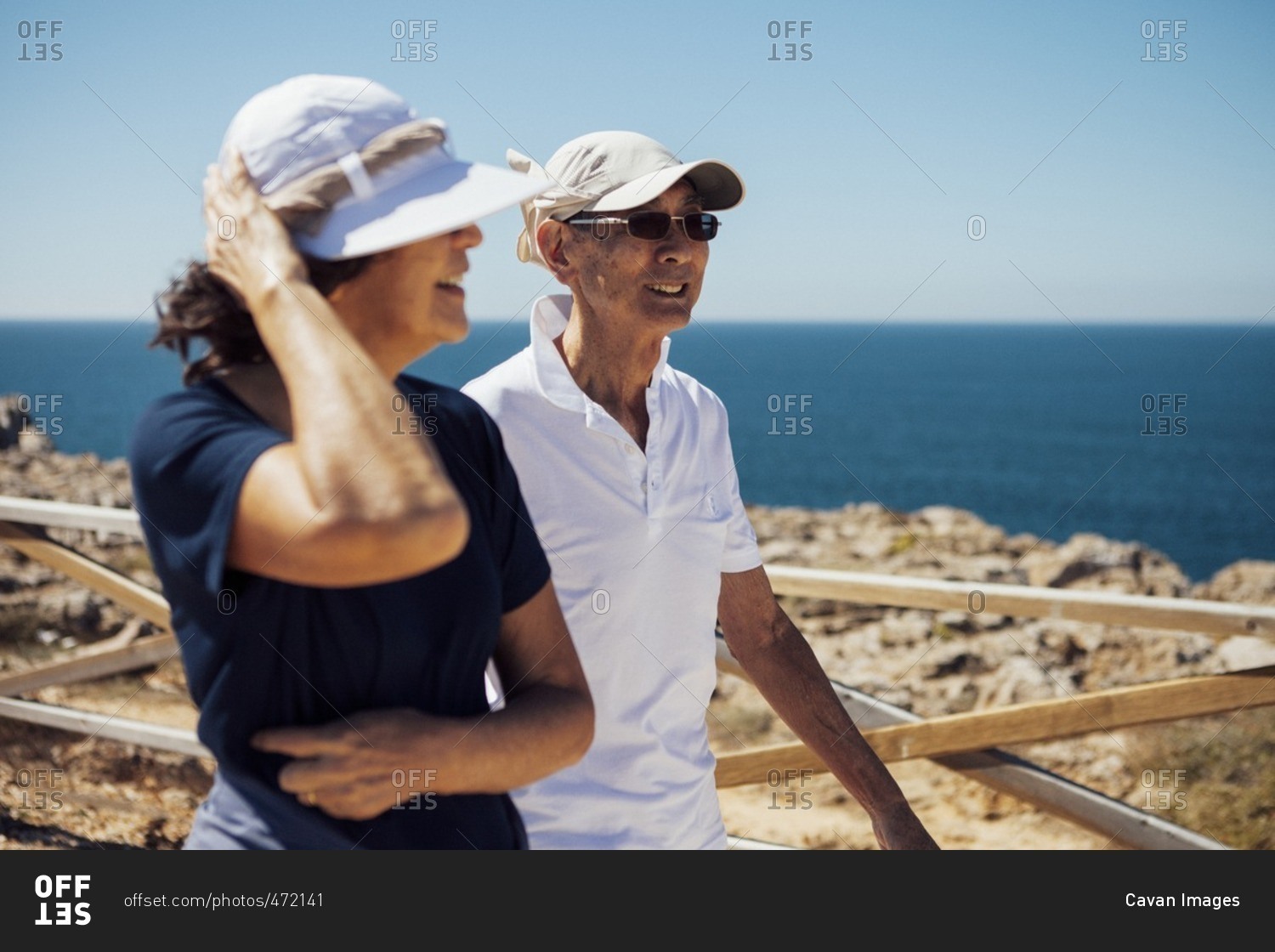 Smiling senior couple looking at sea while standing by railing against clear sky