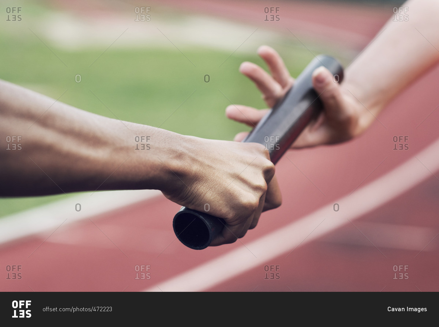 Cropped image of runner passing baton to teammate stock photo OFFSET