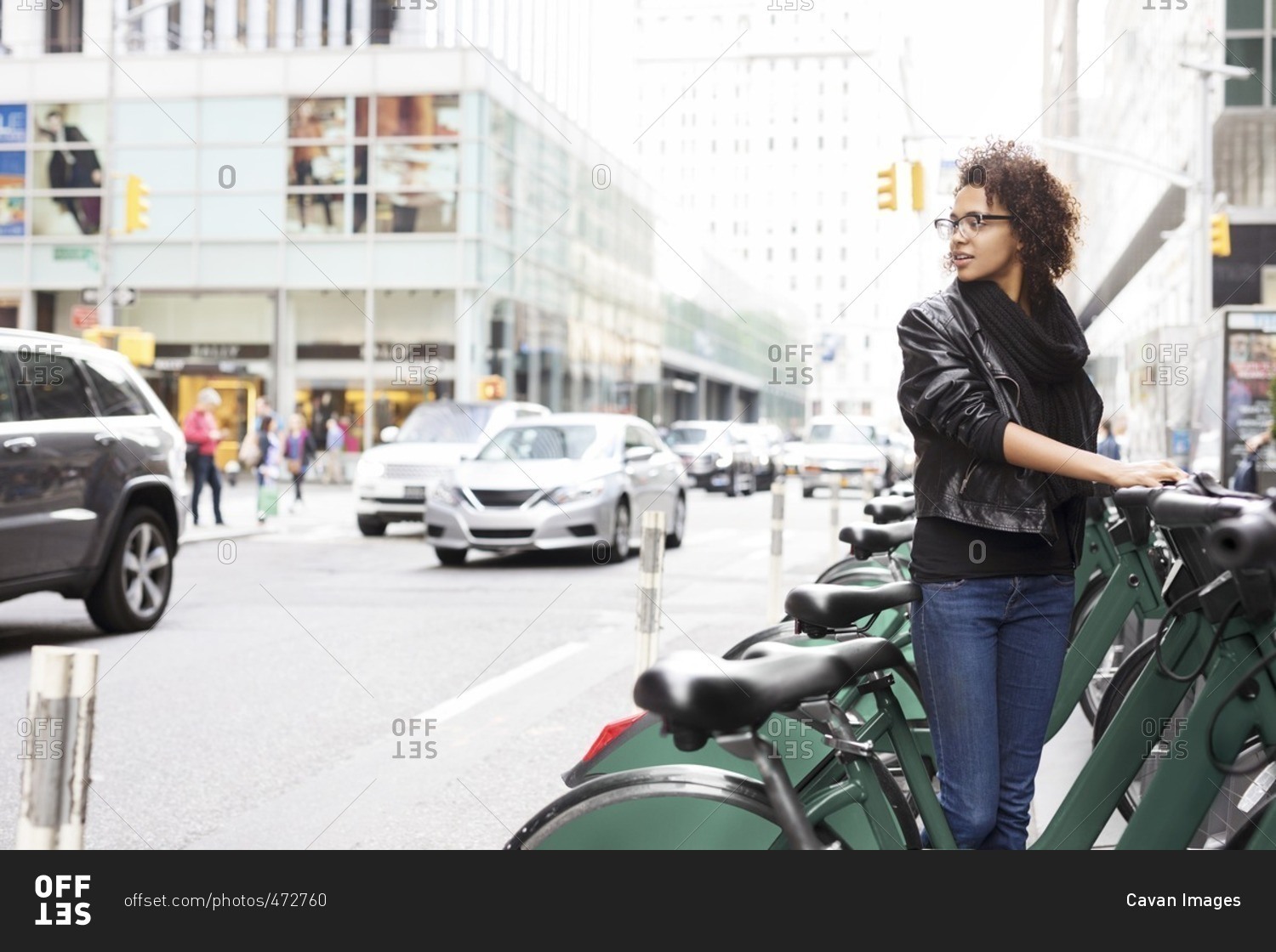 Woman looking away while standing by bicycle rack at parking lot