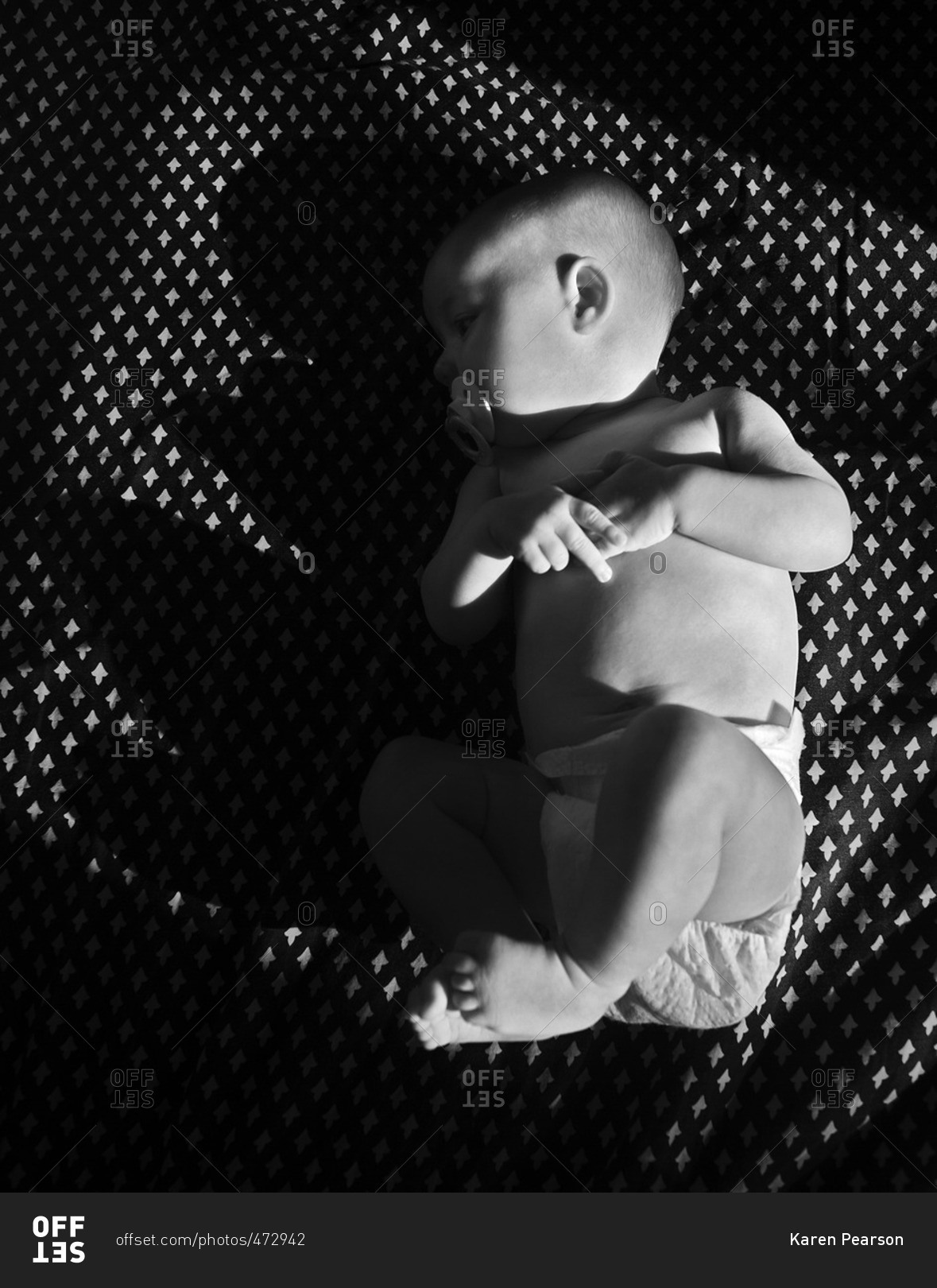 Baby on a patterned sheet with a pacifier in sunlight