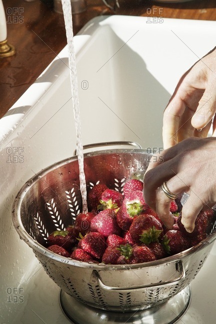 Cropped image of person washing strawberries in kitchen sink