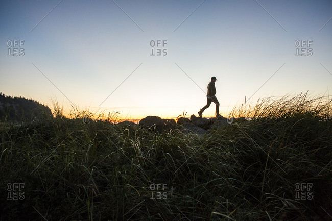 Silhouette of distant Caucasian man walking on rocks at sunset