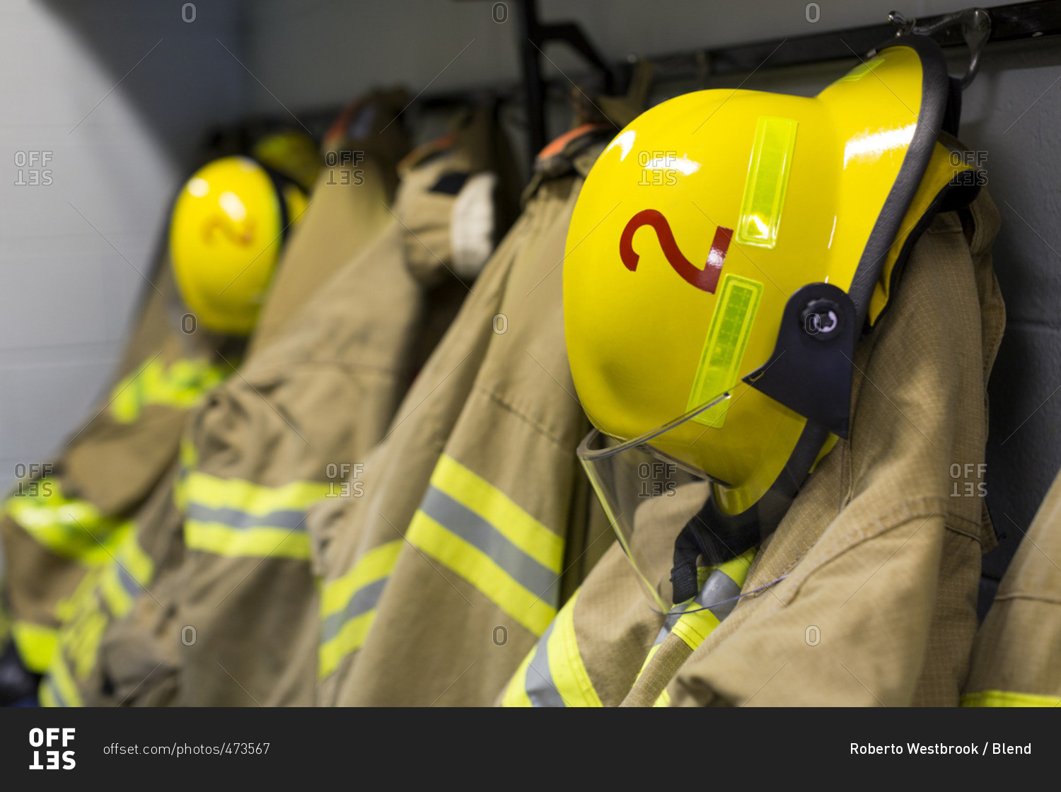 Coats and helmets of fire fighters hanging on hooks stock photo - OFFSET