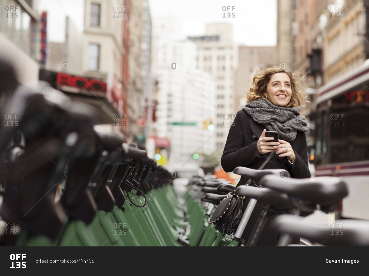 Woman holding mobile phone standing by bicycle rack in city