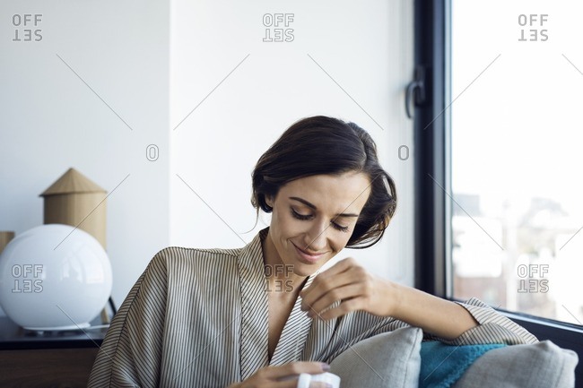 Thoughtful woman dipping teabag in cup while sitting on armchair