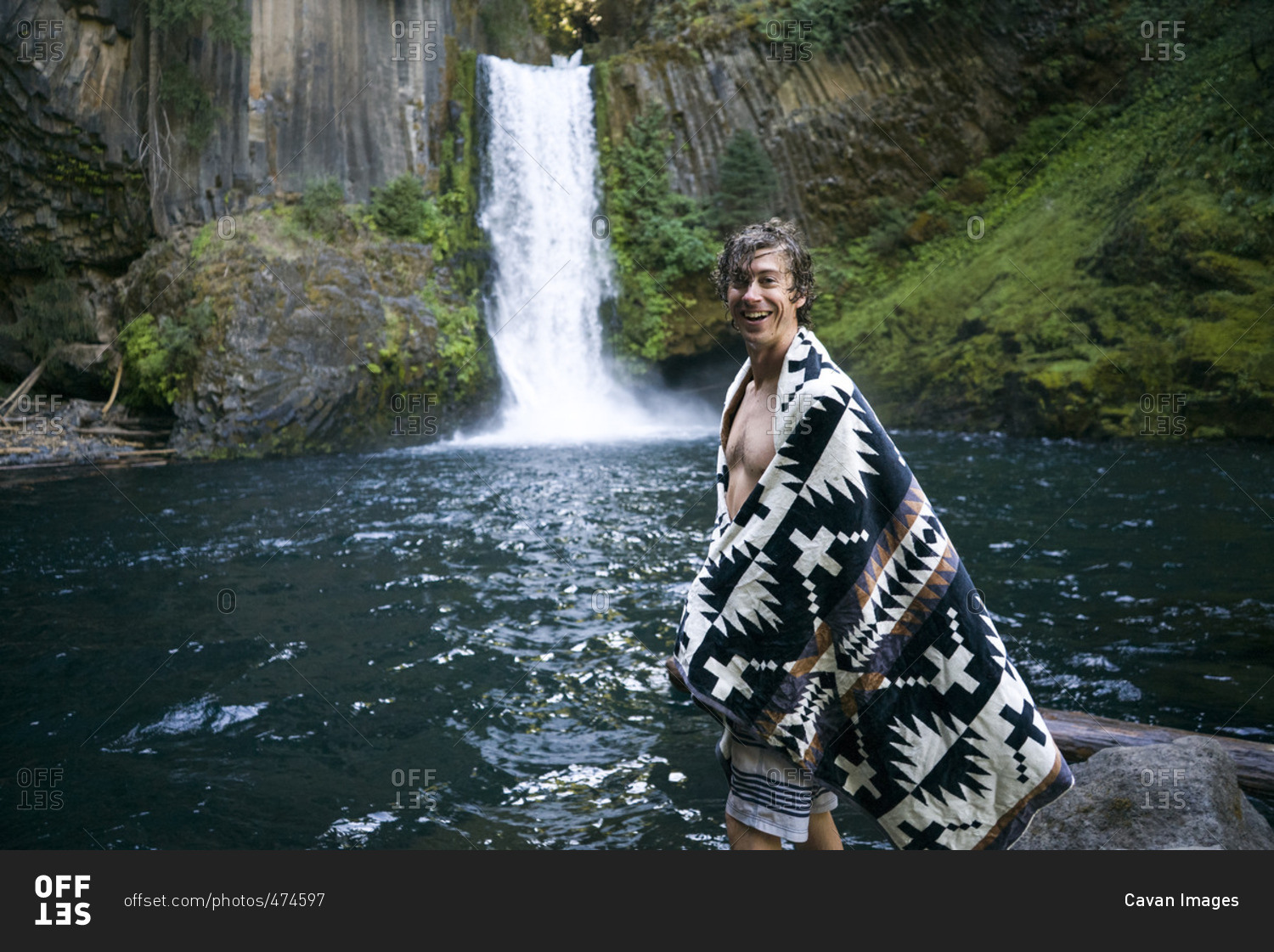 Portrait of happy man in shawl standing by waterfall in forest