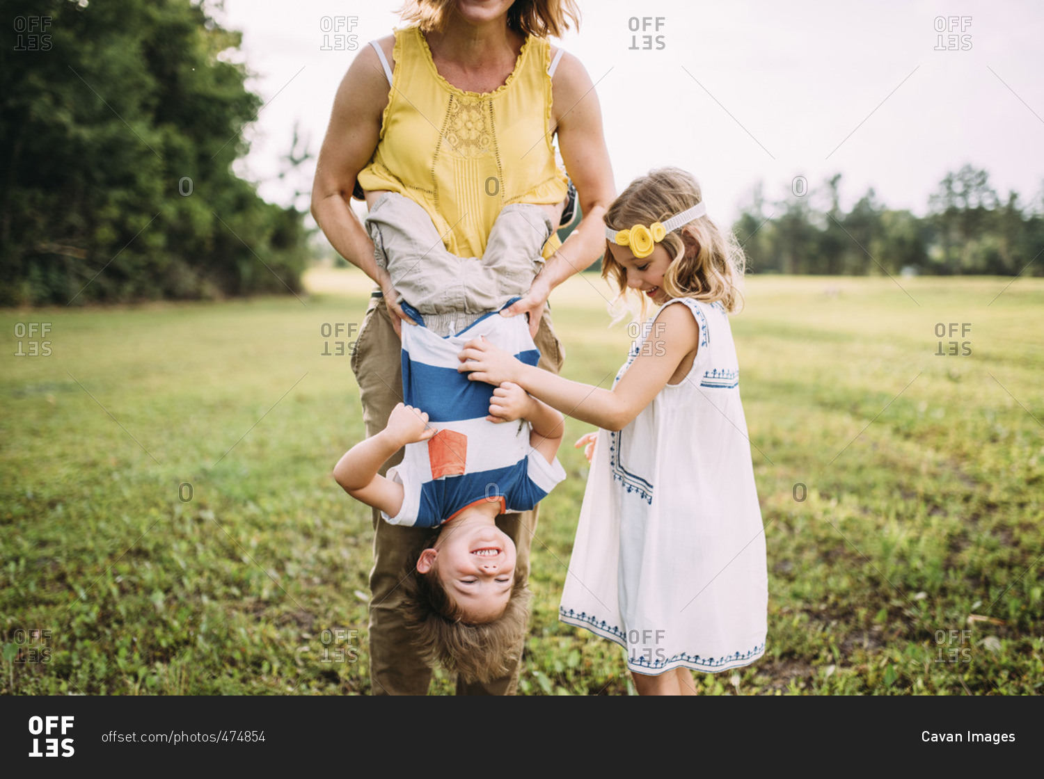 Low section of mother carrying son upside down while standing with daughter at park