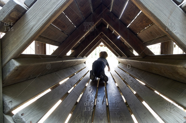 Child crawling in wooden tunnel structure