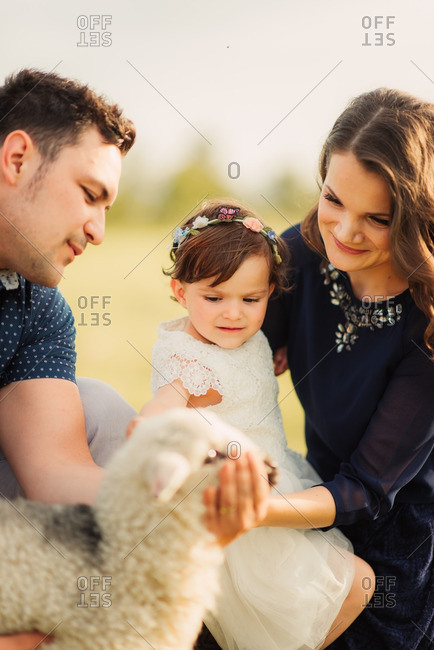 Parents and daughter in a field petting a lamb