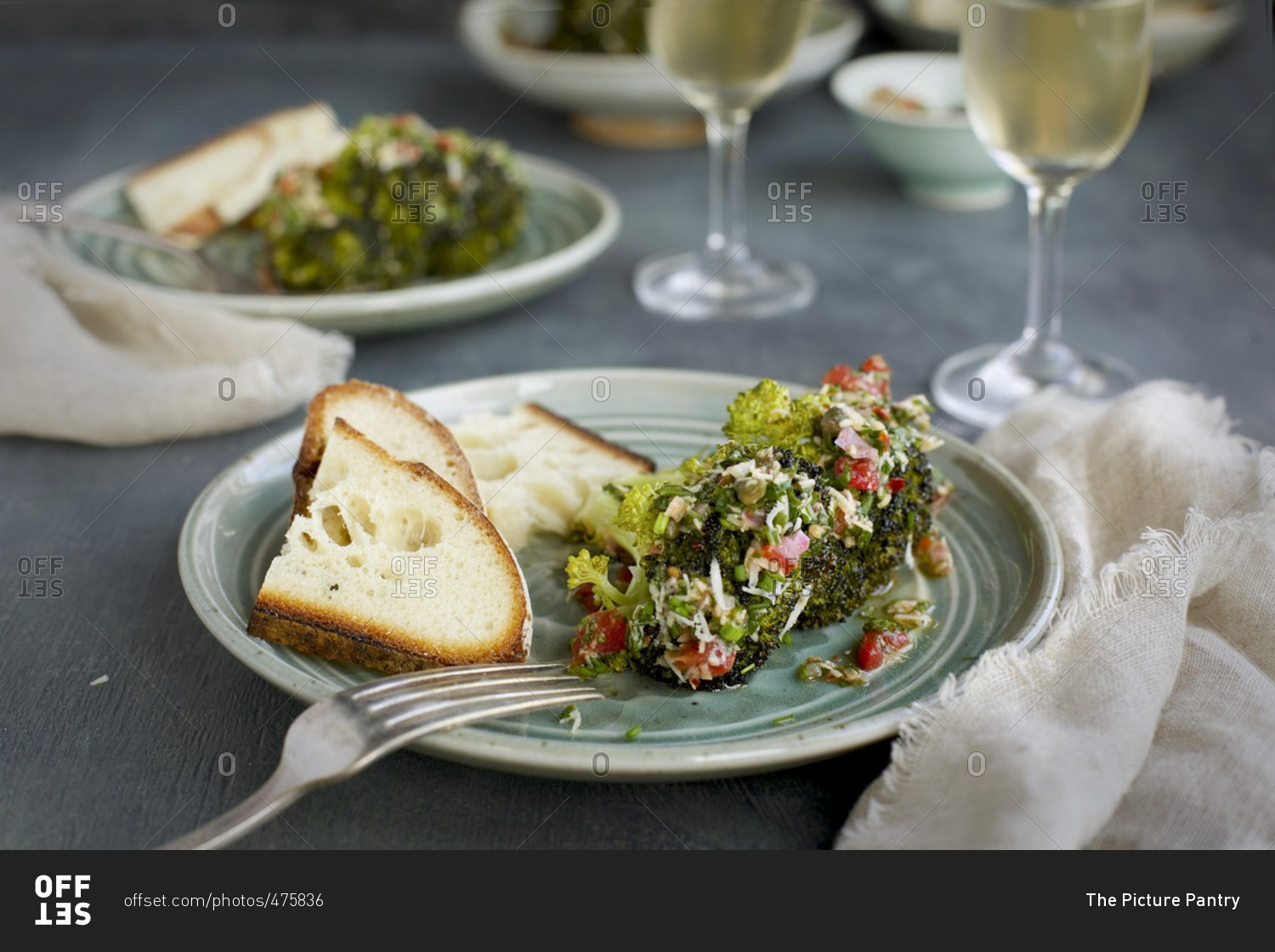 Plates of roasted broccoli with tomatoes and cheese served with bread and white wine