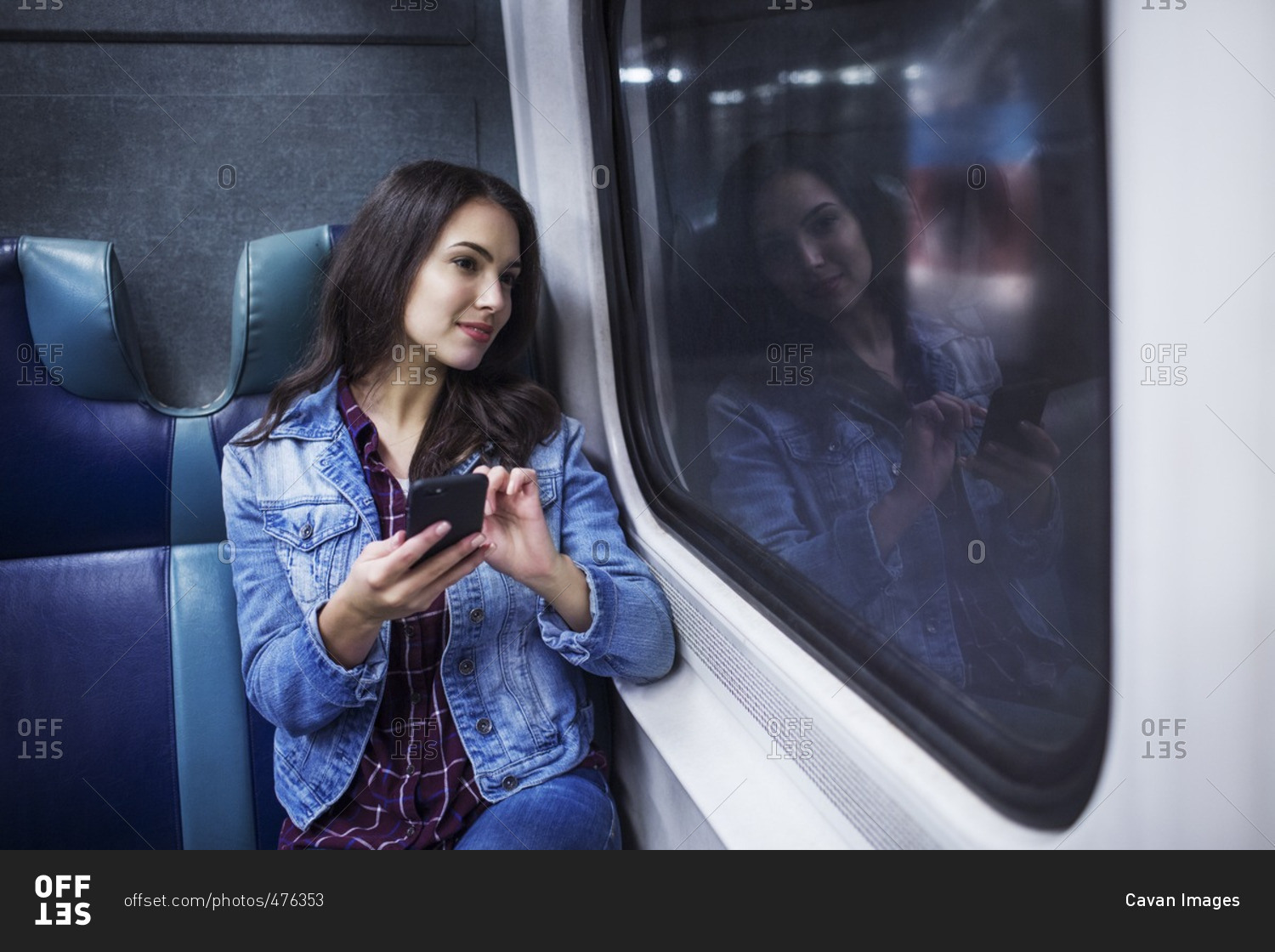 Thoughtful woman with mobile phone looking away while traveling in train