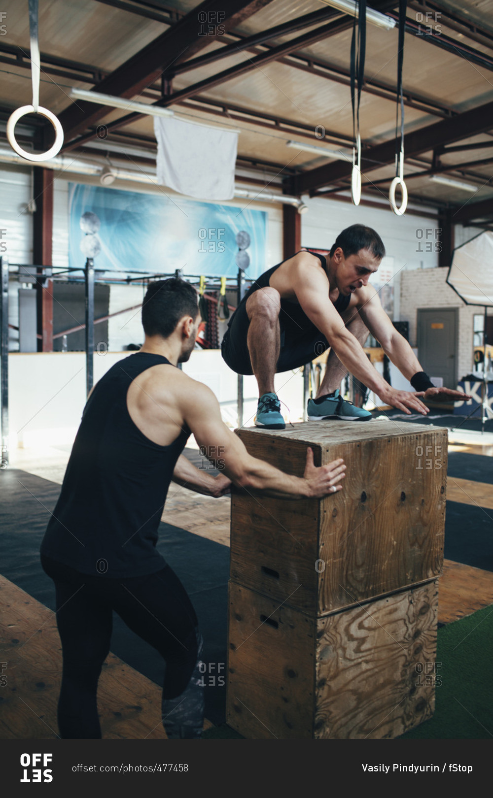 Male athlete assisting friend in doing box jumping at gym