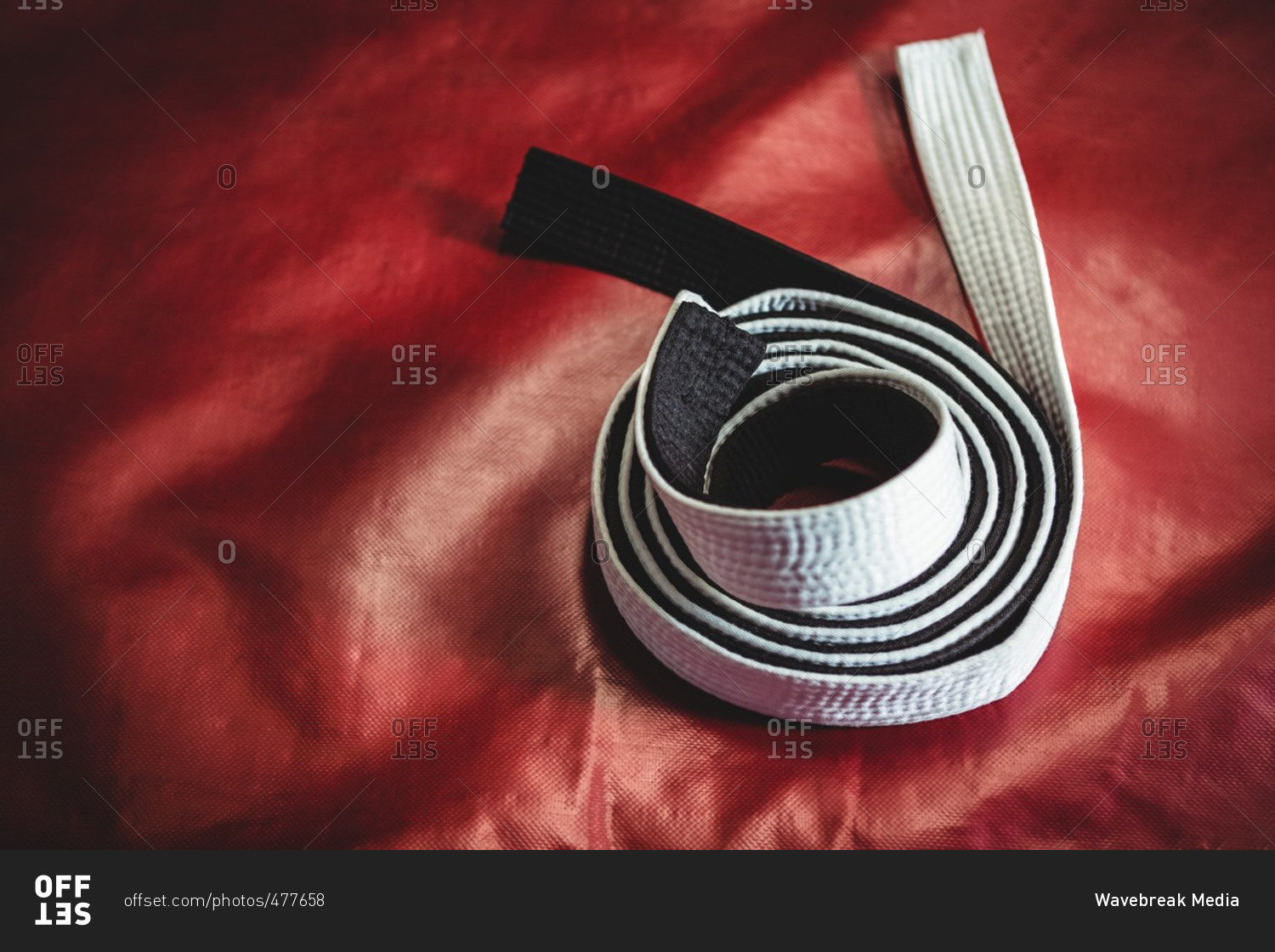 Rolled -up karate white and black belt on red background