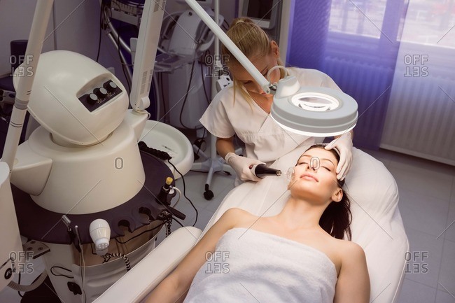 Dermatologist performing laser hair removal on patient face in clinic