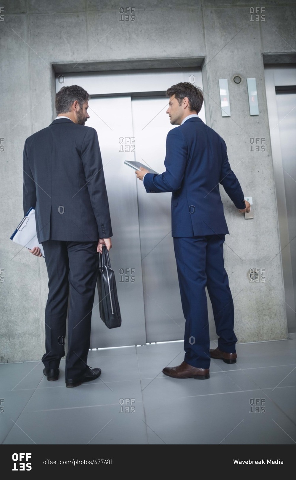 Businessmen standing by lift and pressing button in office