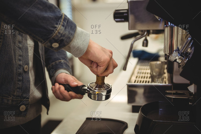 Waiter using a tamper to press ground coffee into a portafilter in cafe 4k  from Pikwizard