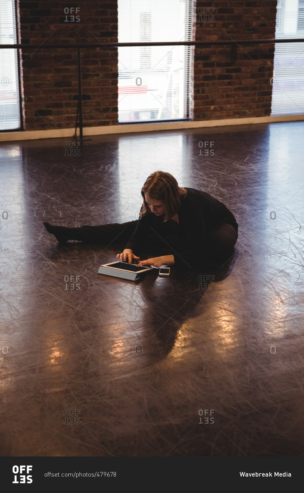 Dancer sitting on floor and using digital tablet in dance studio