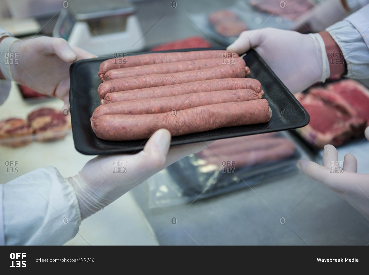 Butchers packing raw sausages in a plastic packaging tray at meat factory