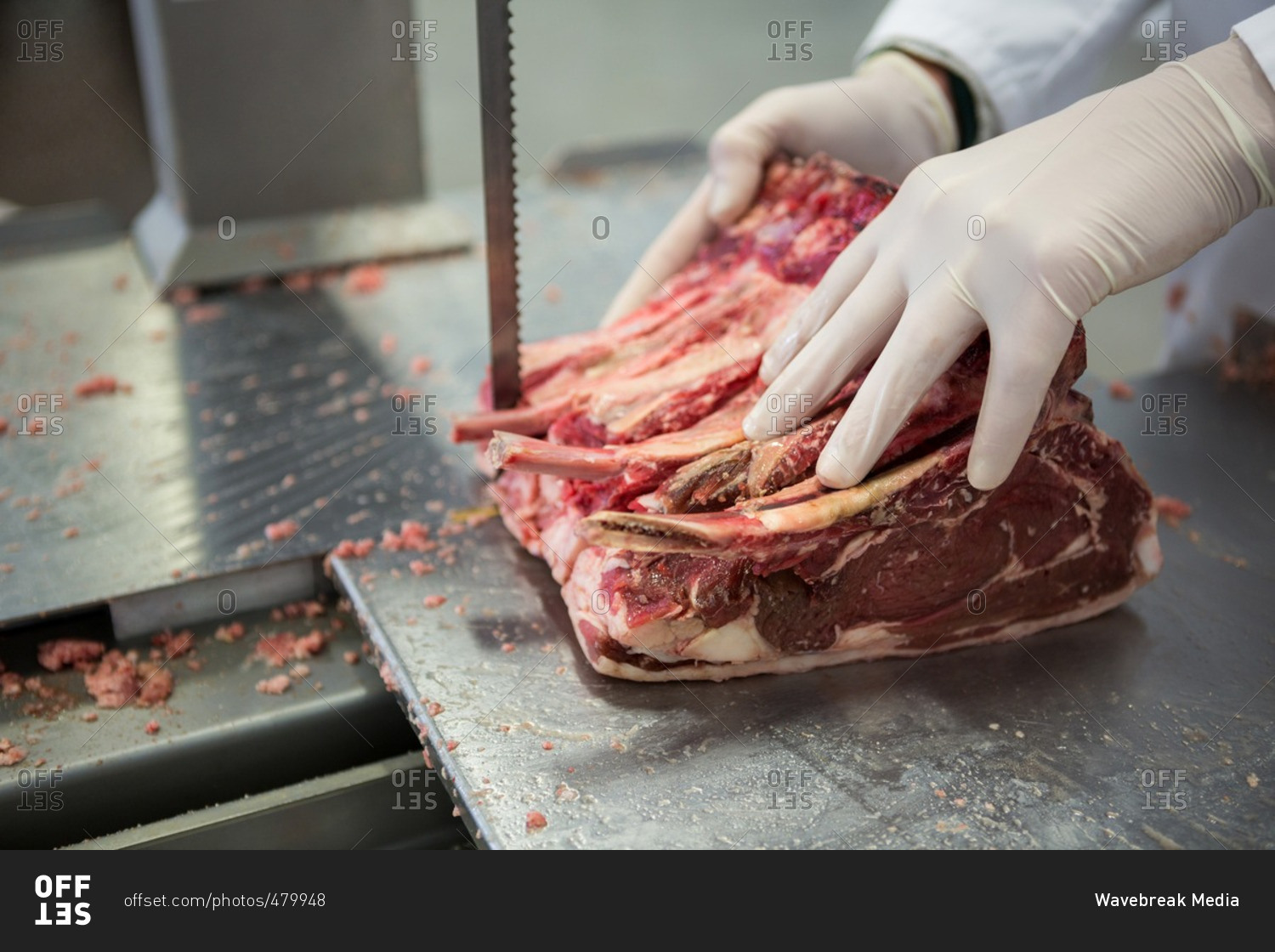 Close-up of butcher cutting raw meat on a band saw machine at meat factory