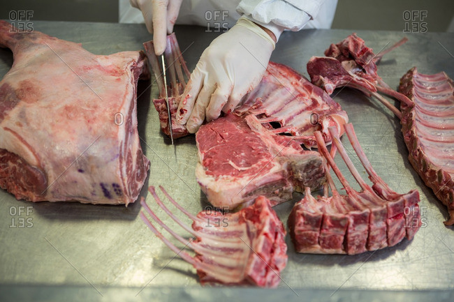 Mid-section of butcher cutting meat at meat factory