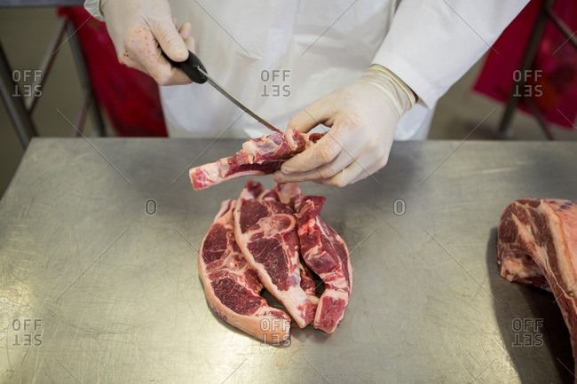 Mid-section of butcher cutting meat at meat factory