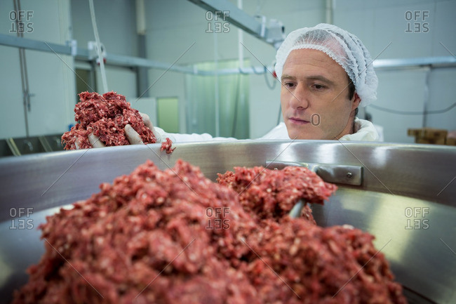 Butcher putting meat in mincer machine at meat factory