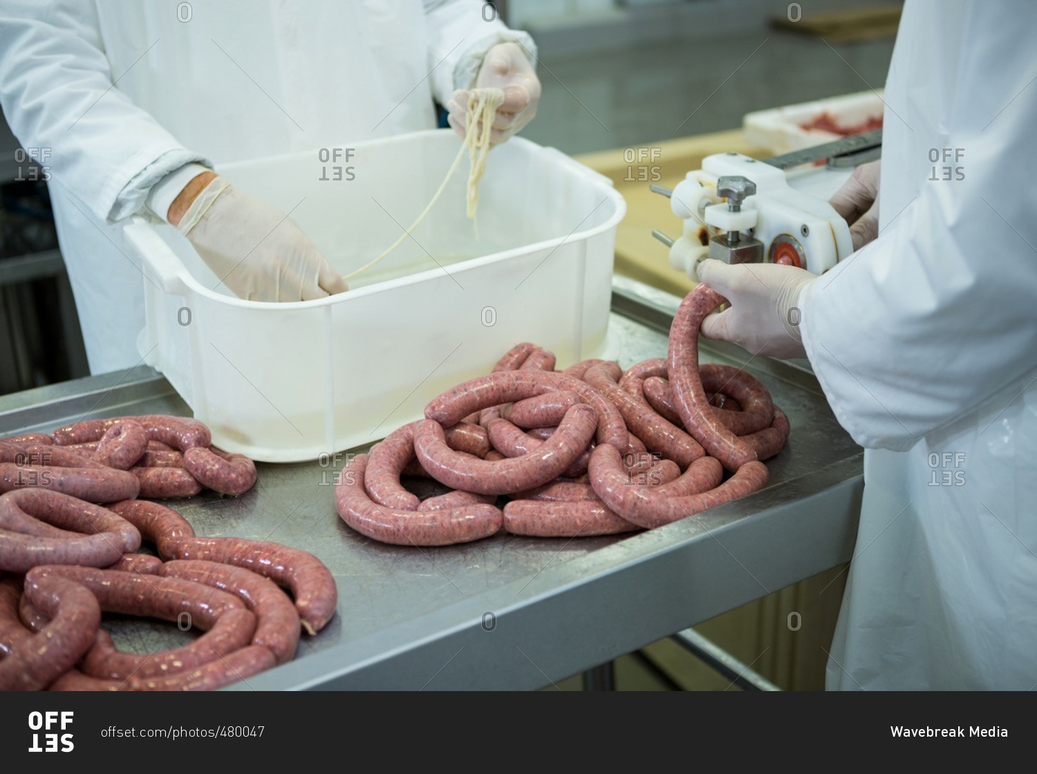 Mid-section of butchers processing sausages in meat factory