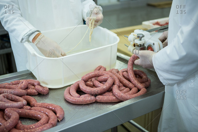 Mid-section of butchers processing sausages in meat factory