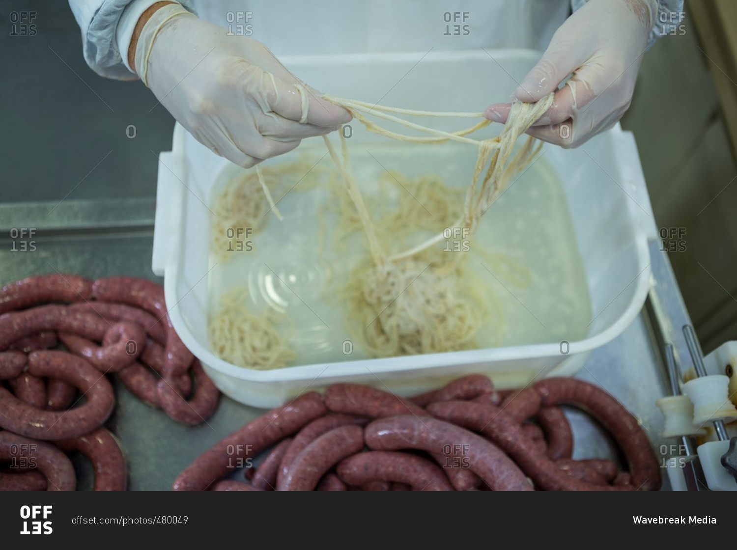 Mid-section of butcher processing sausages in meat factory