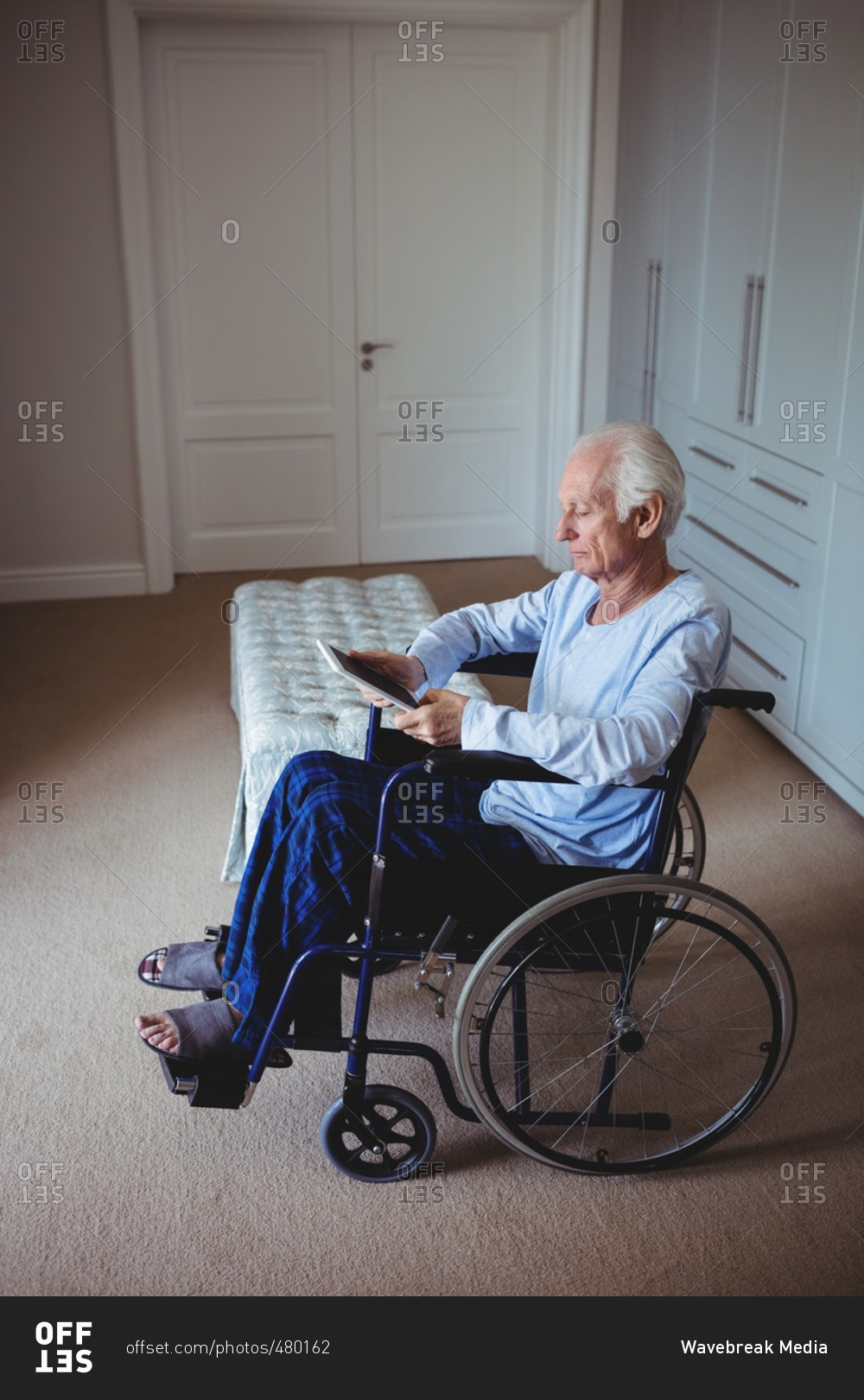 Senior man sitting on wheelchair and using digital tablet at home