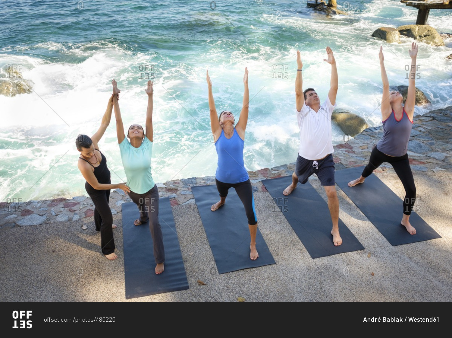 Instructor helping group doing yoga at ocean front