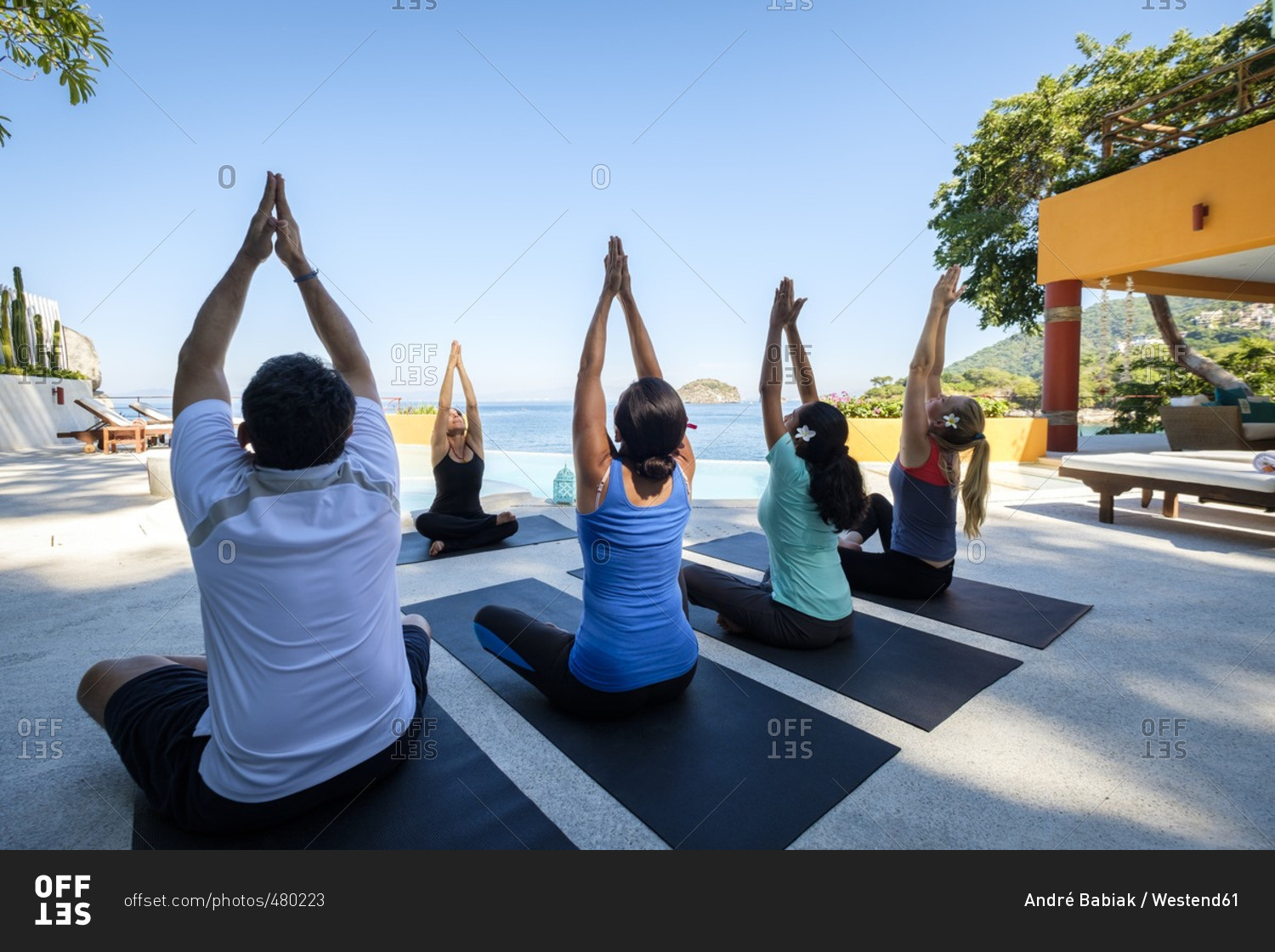 Yoga group with teacher exercising at ocean front villa