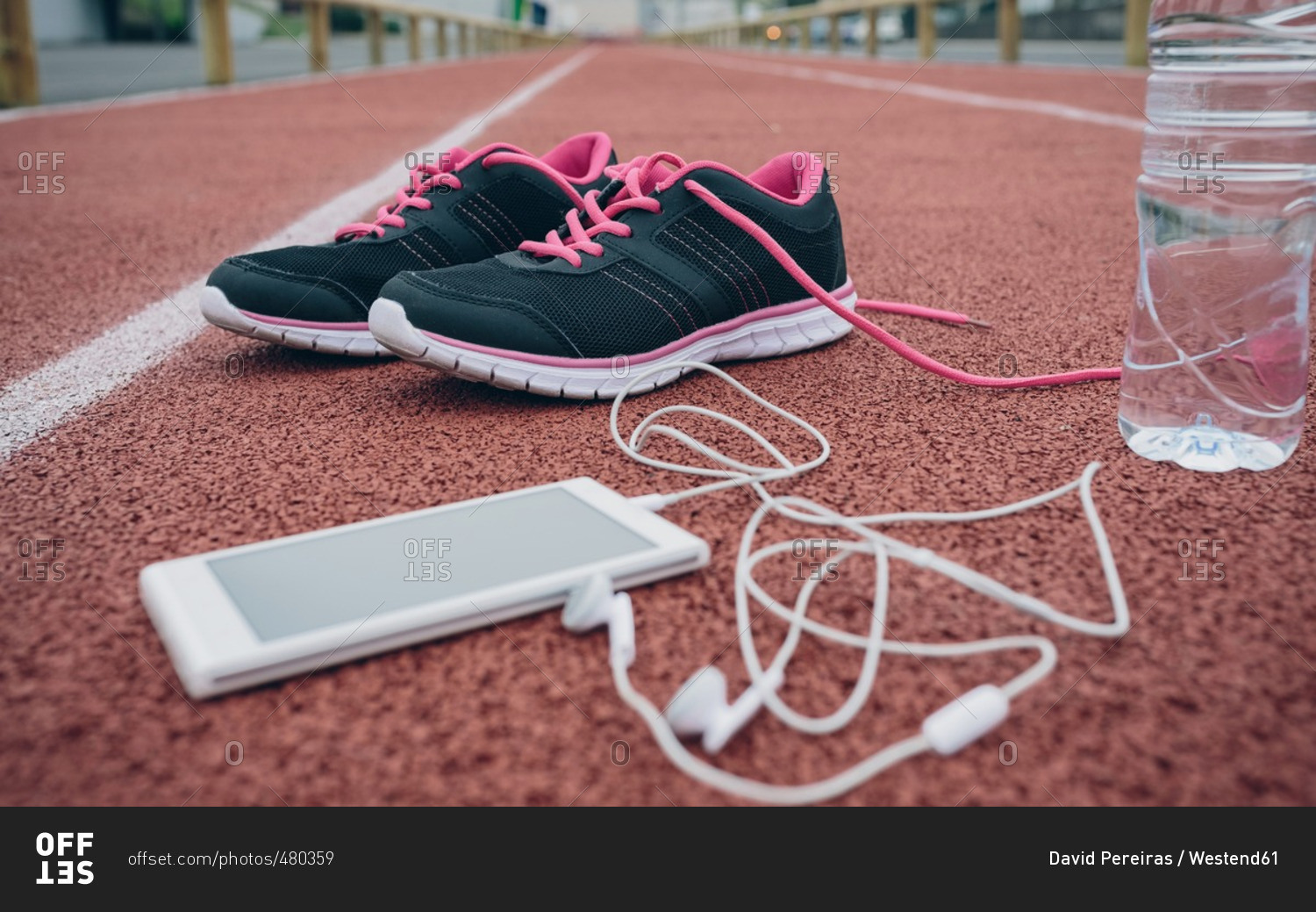 Sport shoes- smartphone with earbuds and bottle of water on tartan track