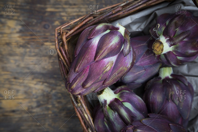 Basket of purple organic artichokes on dark wood