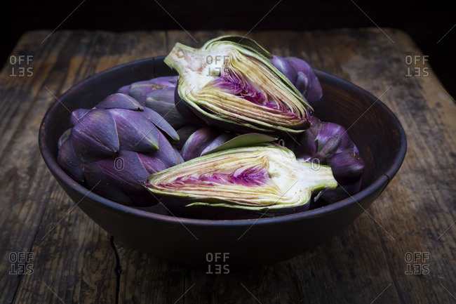 Bowl of purple organic artichokes on dark wood
