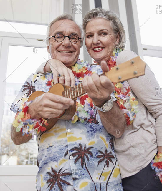 Happy senior couple with man in Hawaiian shirt playing ukulele