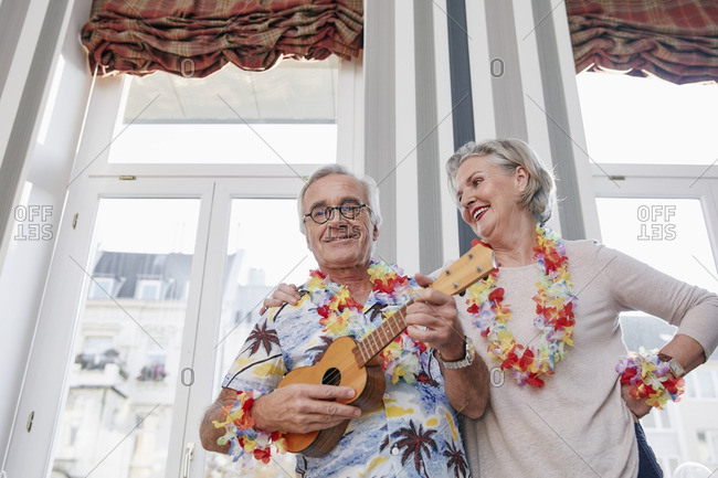 Happy senior couple with man in Hawaiian shirt playing ukulele