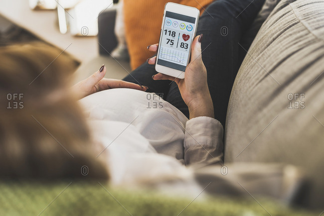 Pregnant woman on couch using smartphone checking health data