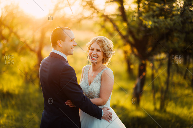 Grinning bride with groom in sunlight