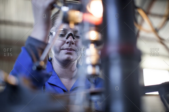 Woman wearing protective glasses operating machine in workshop