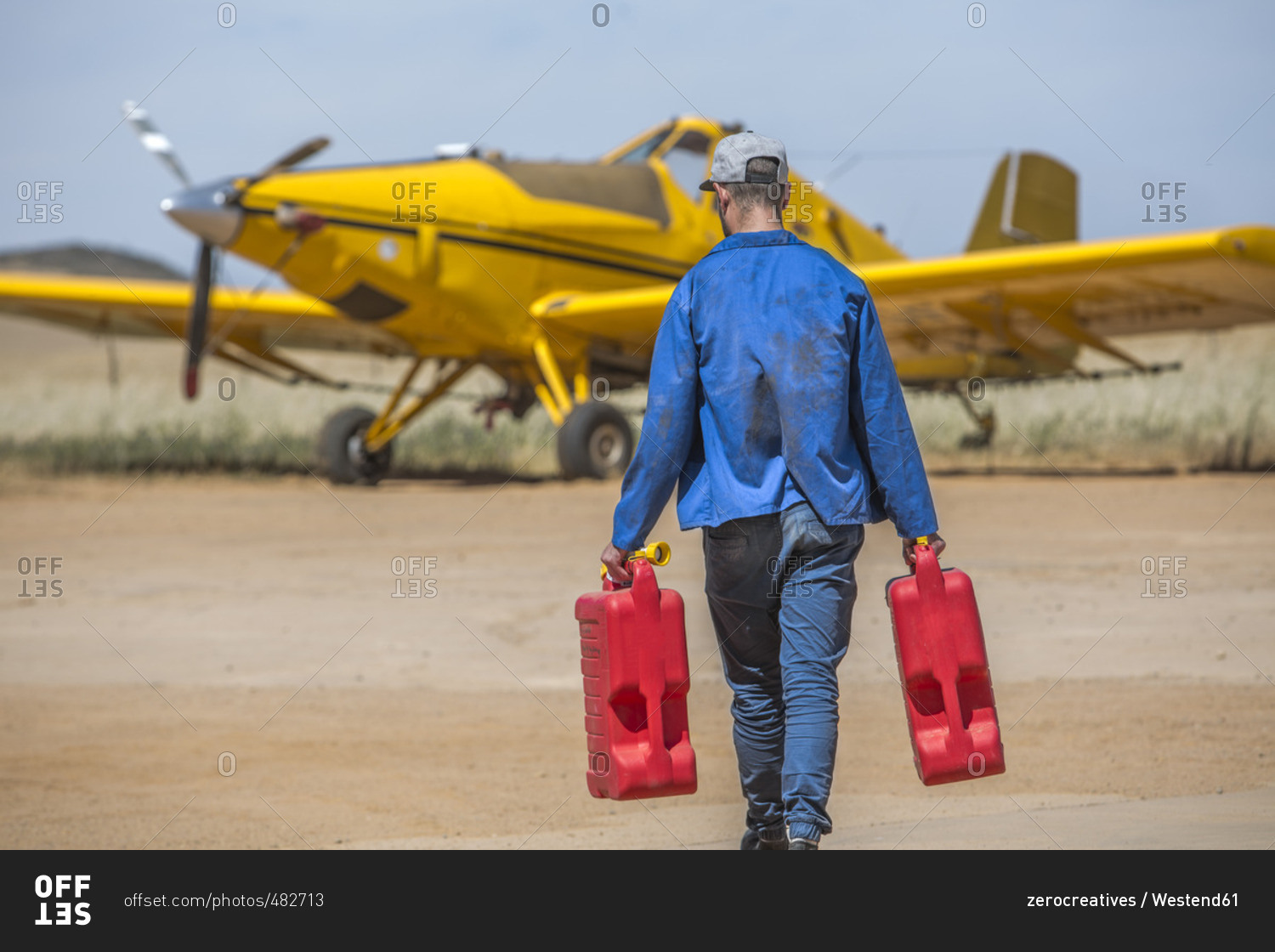 Mechanic carrying jerry cans towards yellow crop dusting plane