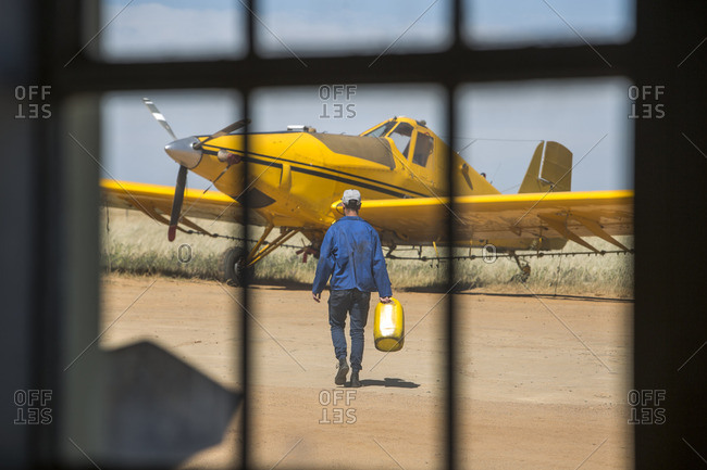 Mechanic carrying jerry cans towards yellow crop dusting plane
